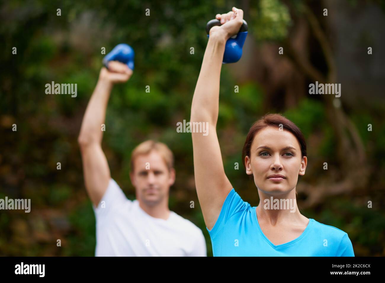 Faites de l'exercice à l'air frais. Prise de vue d'un homme et d'une femme utilisant des poids de cloche de bouilloire lors d'un cours d'exercice en plein air. Banque D'Images