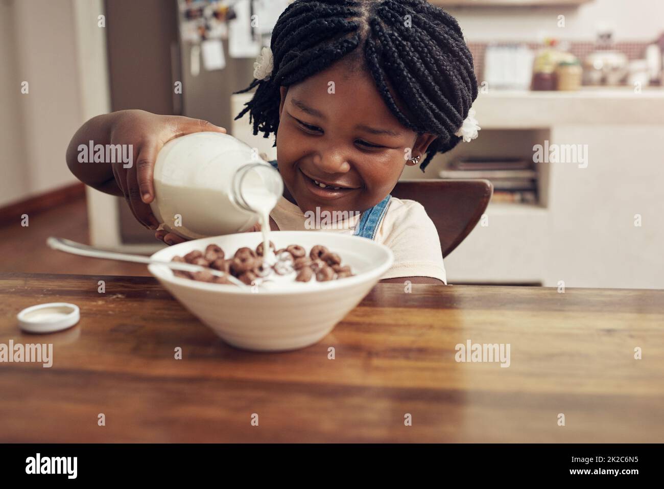 J'aime mes petits déjeuners très laiteux. Un petit cliché d'une adorable petite fille qui verse du lait dans son bol à céréales à la maison. Banque D'Images