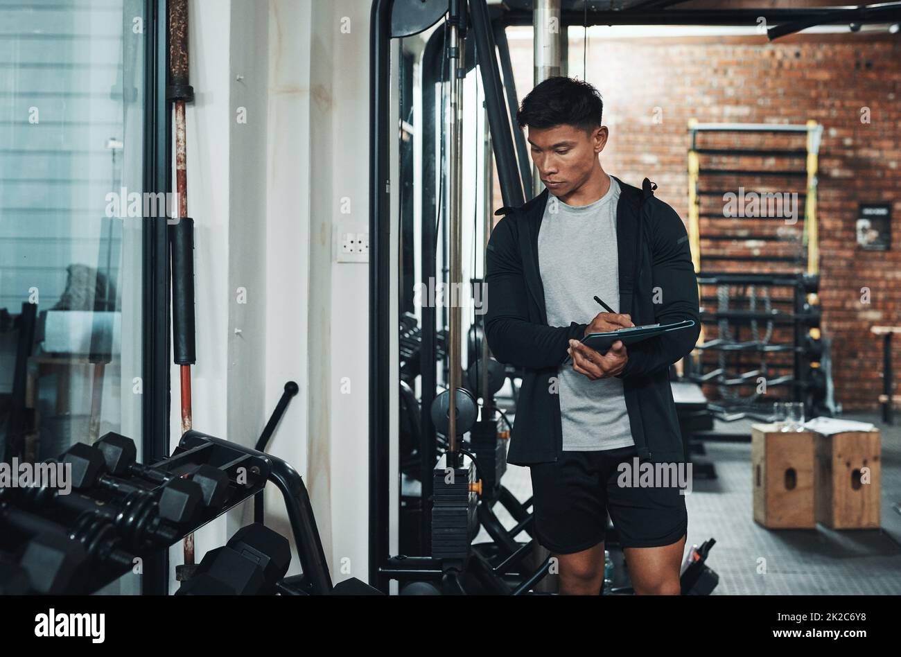 Je pense que j'en aurais besoin Plan court d'un beau jeune homme instructeur de fitness inspectant l'équipement d'exercice tout en travaillant dans une salle de gym. Banque D'Images