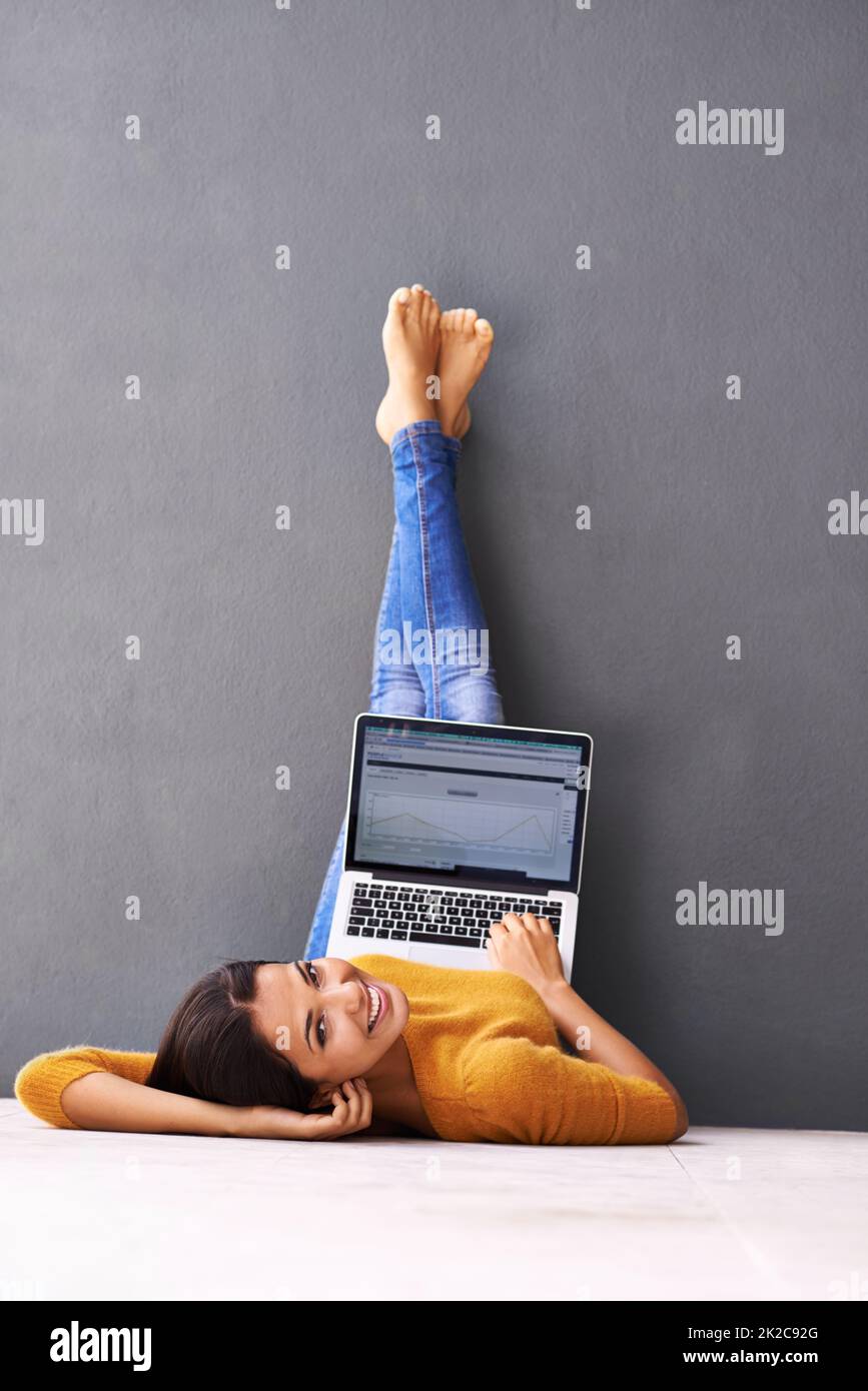 L'aspect supérieur de la technologie. Une jeune femme couchée sur le sol avec son ordinateur portable sur fond gris. Banque D'Images