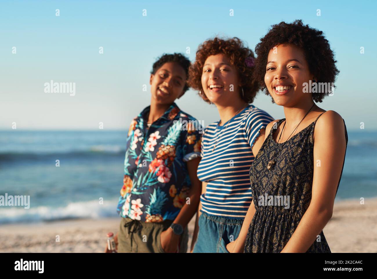 Nous nous faisons sourire les uns les autres. Portrait de trois jeunes femmes attrayantes debout ensemble et posant sur la plage pendant la journée. Banque D'Images