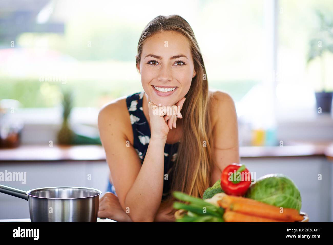 Évitez le régime, juste manger sain. Portrait d'une jeune femme penchée sur son comptoir de cuisine avec un pot et des légumes à côté d'elle. Banque D'Images