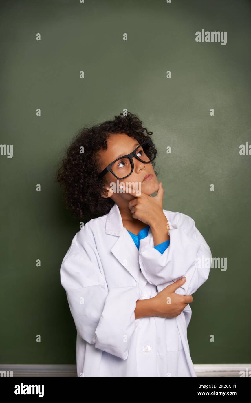 Rêver de son brillant avenir. Un garçon ethnique portant des lunettes et un manteau de laboratoire regardant contemplatif - copyspace. Banque D'Images