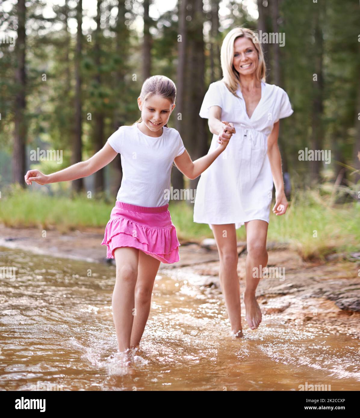 Allons-y de cette façon maman. Une petite fille mignonne qui court dans un ruisseau sauvage avec sa mère. Banque D'Images