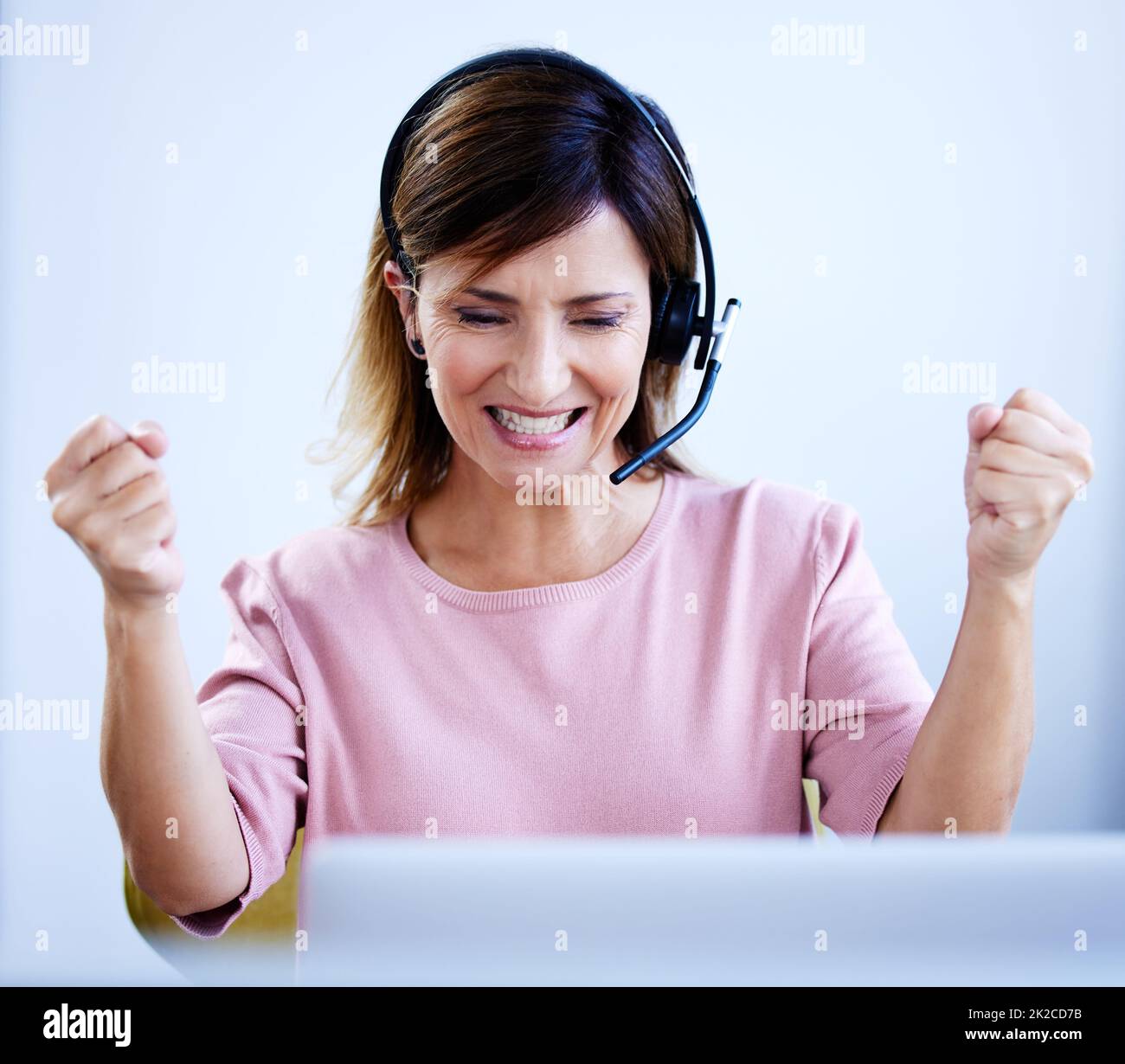 Gagner dans le jeu de vente. Photo d'un agent de centre d'appels mature qui applaudisse tout en travaillant sur un ordinateur portable dans un bureau. Banque D'Images