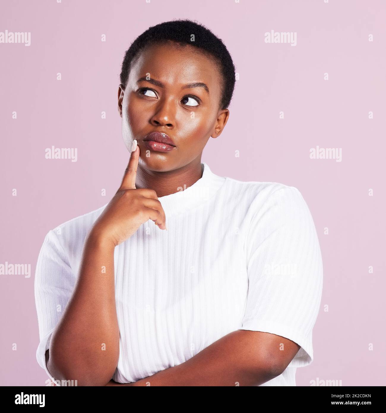 Donnez-moi une seconde pour réfléchir. Photo en studio d'une jeune femme regardant contemplative sur fond rose. Banque D'Images