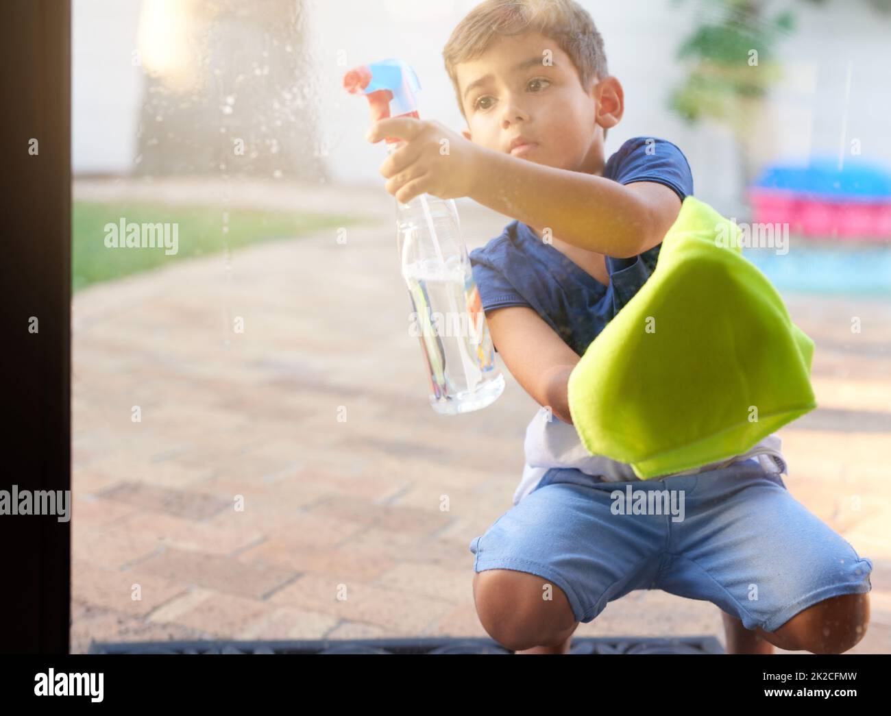 Fait partie de l'équipe de nettoyage du printemps. Photo d'un petit garçon lavant une porte en verre à la maison. Banque D'Images