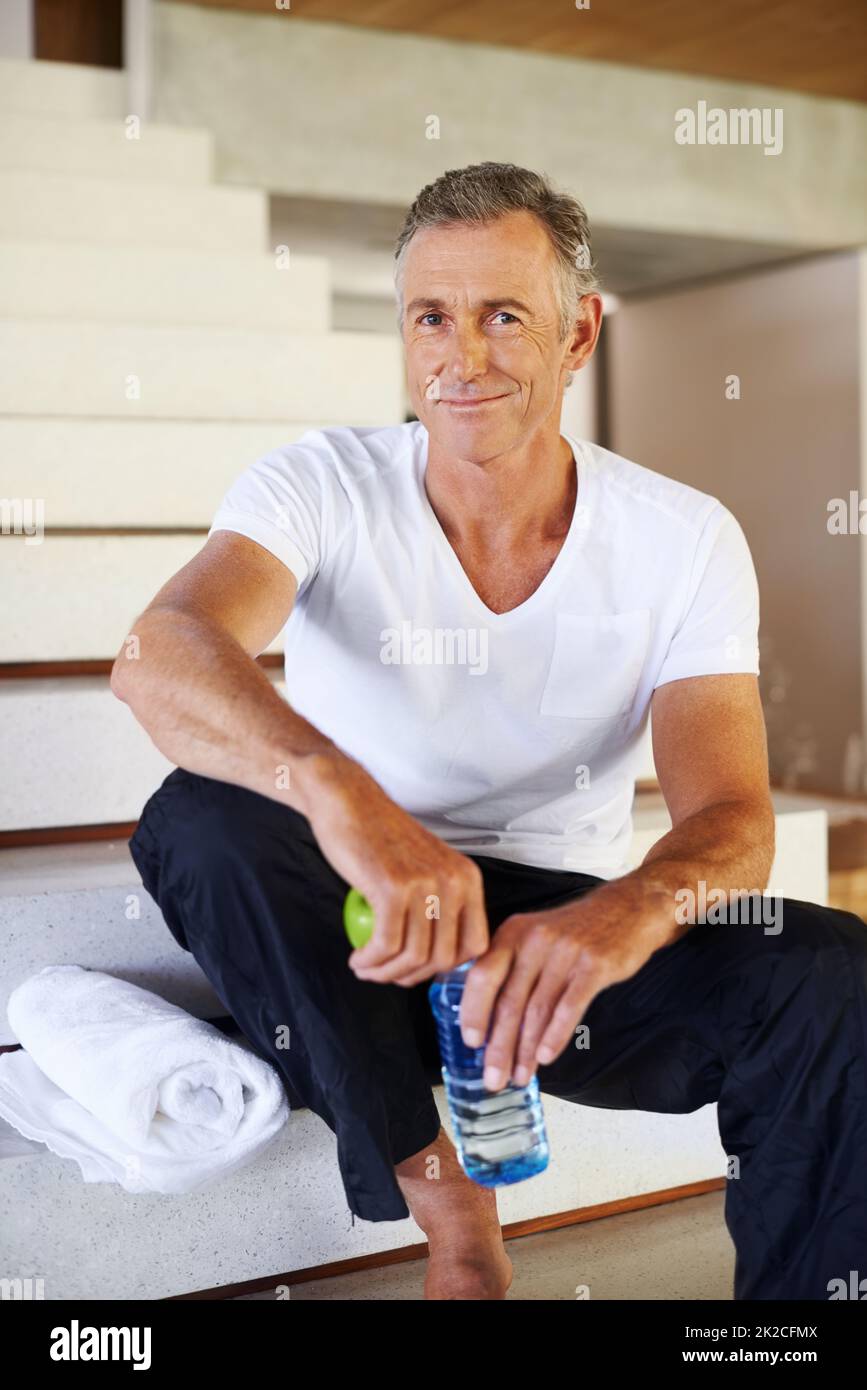 Détente et sensation de bien-être. Un beau homme mûr se détendant à la maison avec une pomme et une bouteille d'eau. Banque D'Images