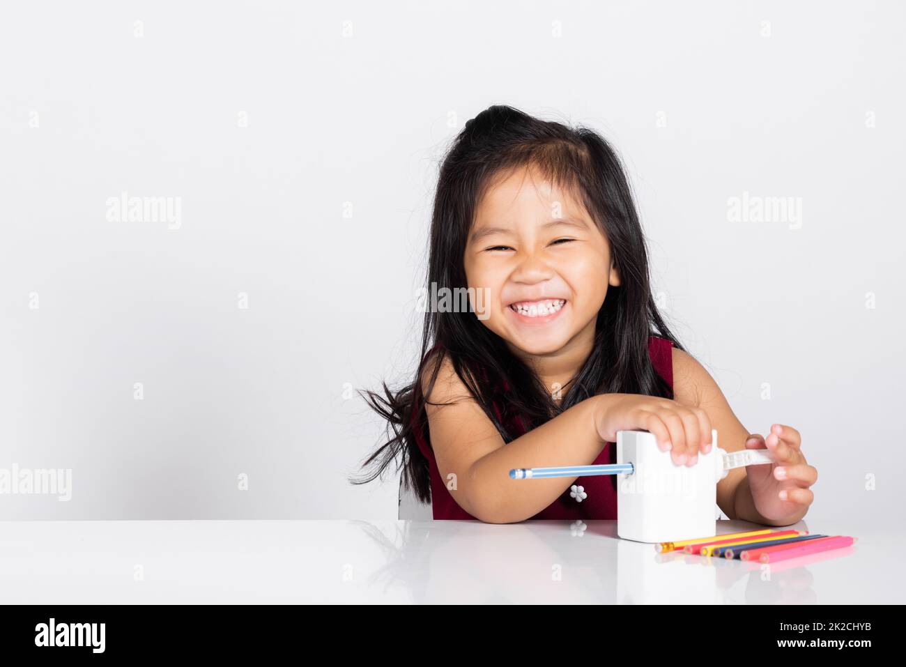 Petite petite petite fille mignonne 3-4 ans sourire à l'aide d'un taille-crayon tout en faisant des devoirs en studio photo isolée Banque D'Images