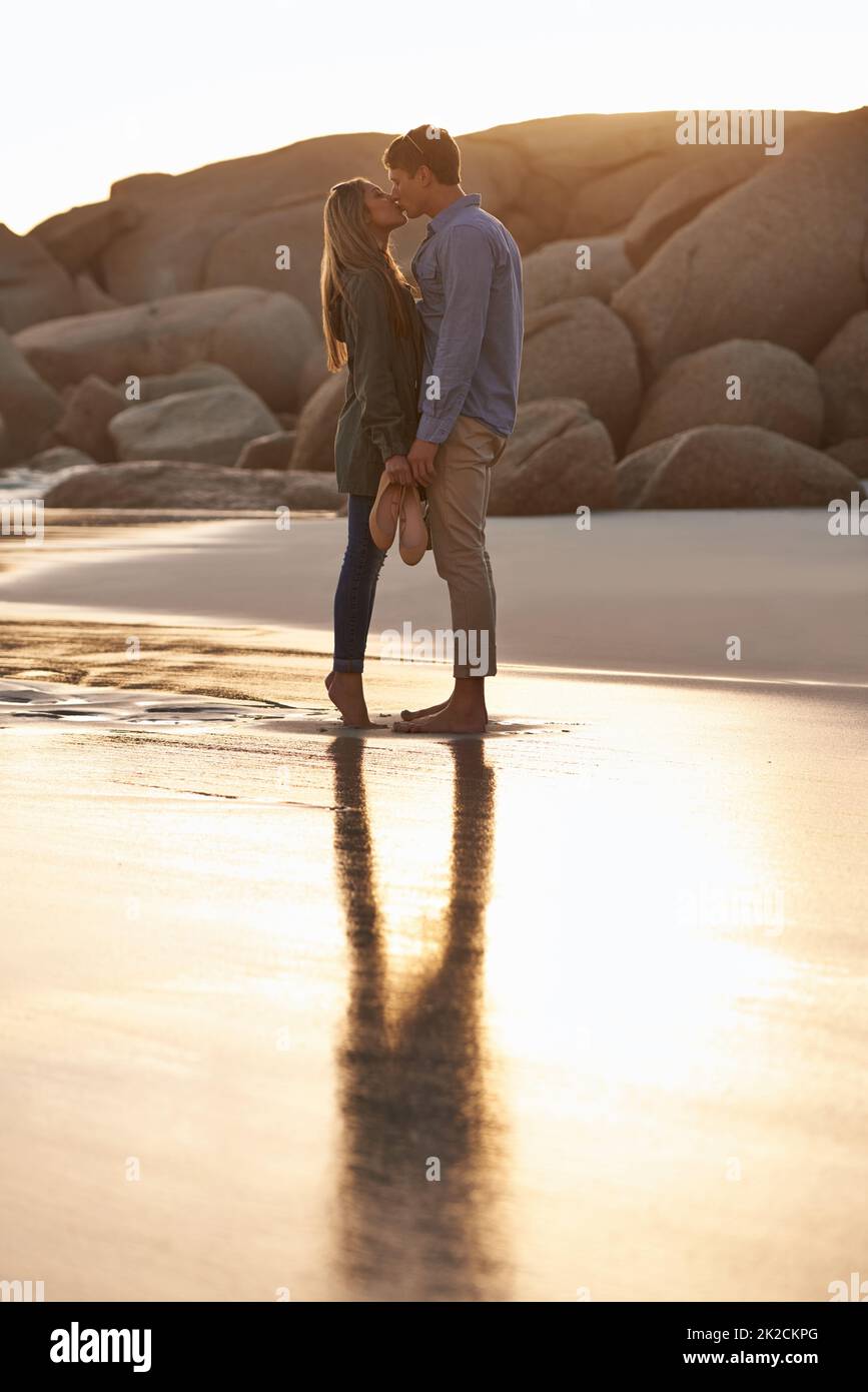 Lèvre verrouillée. Photo d'un jeune couple en train de profiter d'un baiser romantique sur la plage au coucher du soleil. Banque D'Images