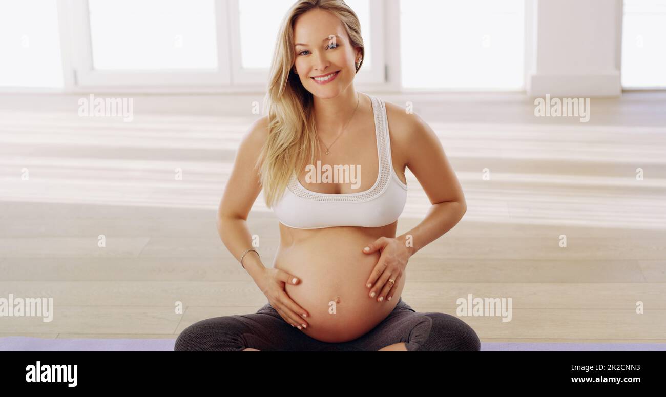 Rester en bonne santé pour le bébé. Portrait court d'une jeune femme enceinte attirante frottant contre la bosse de son bébé tout en étant assise sur un tapis de yoga. Banque D'Images