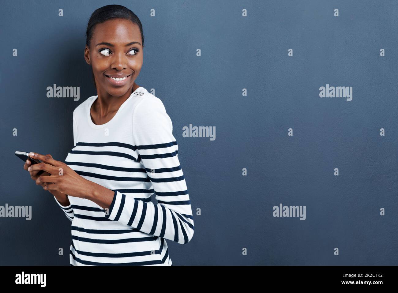 Envoyer des SMS sur le malicieux. Photo d'une jeune femme attrayante utilisant son téléphone sur un fond gris. Banque D'Images