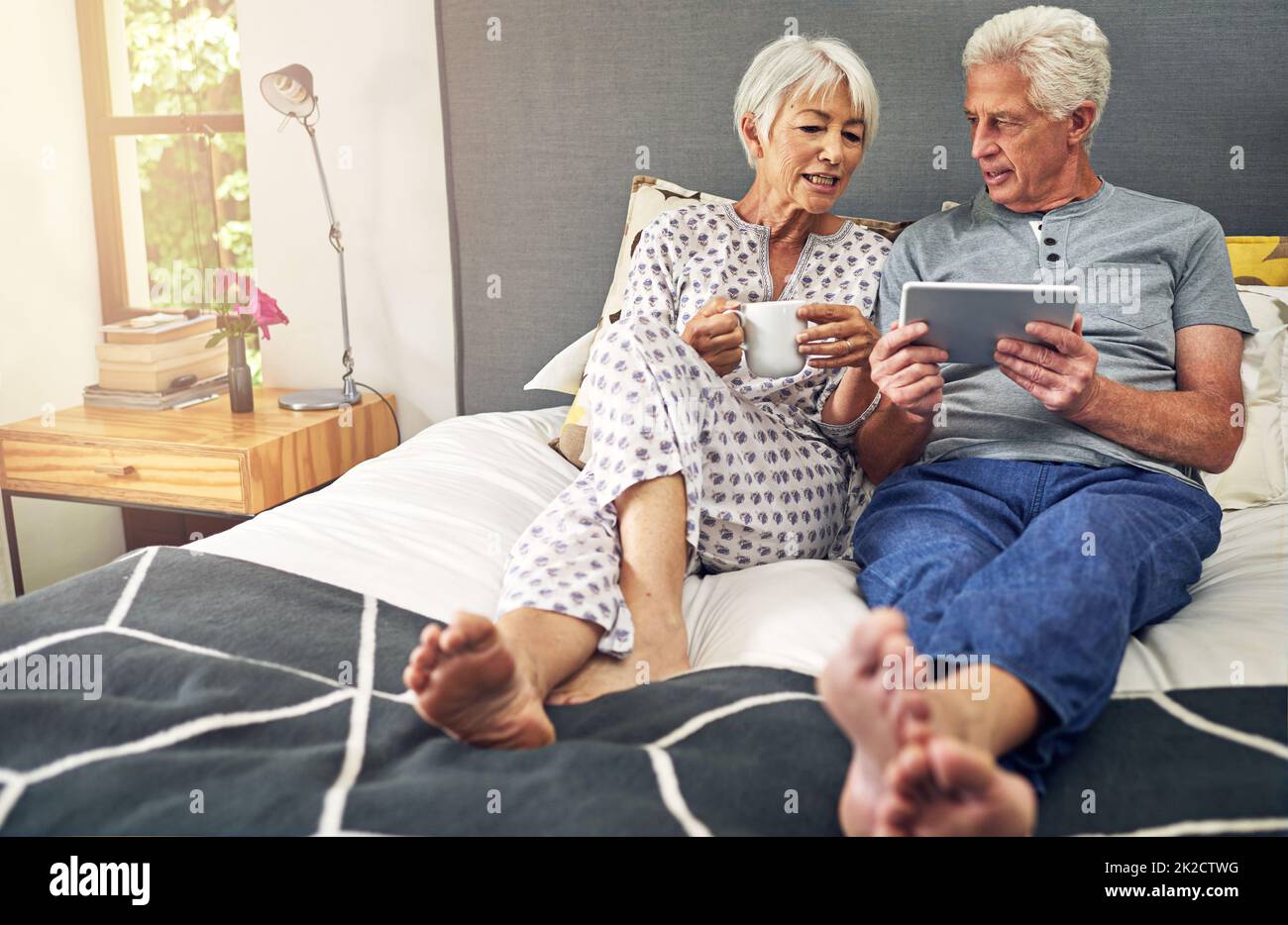 Permet de réserver des vacances en ligne. Prise de vue d'un couple âgé utilisant une tablette tout en étant allongé dans le lit. Banque D'Images