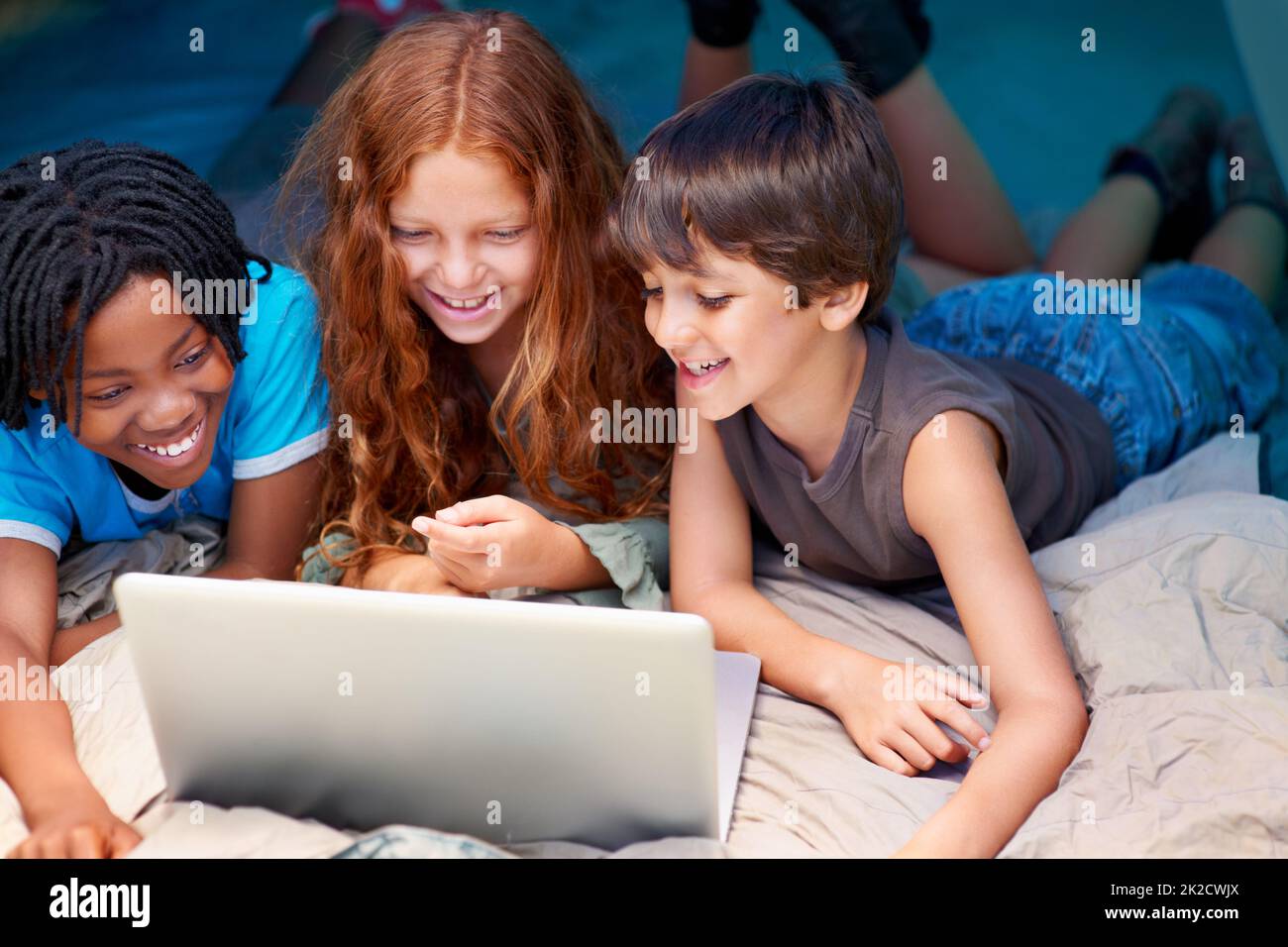 Toujours connecté, où qu'ils se trouvent - technologie moderne. Les enfants s'amusent à utiliser un ordinateur portable pendant qu'ils campent dans une tente. Banque D'Images