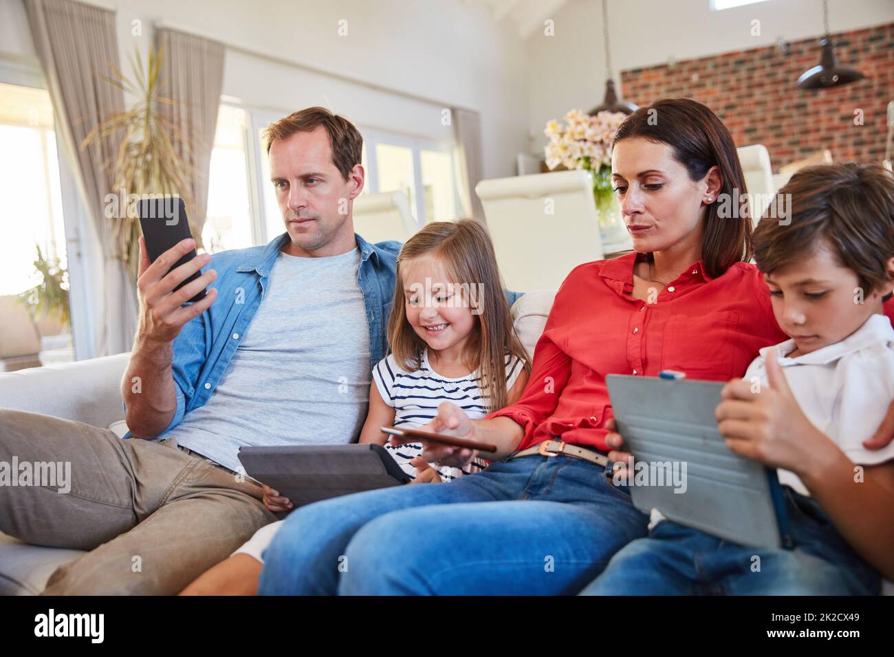 Distractions numériques. Photo d'une jeune famille assise sur le canapé de son salon, distraite par divers médias et appareils. Banque D'Images