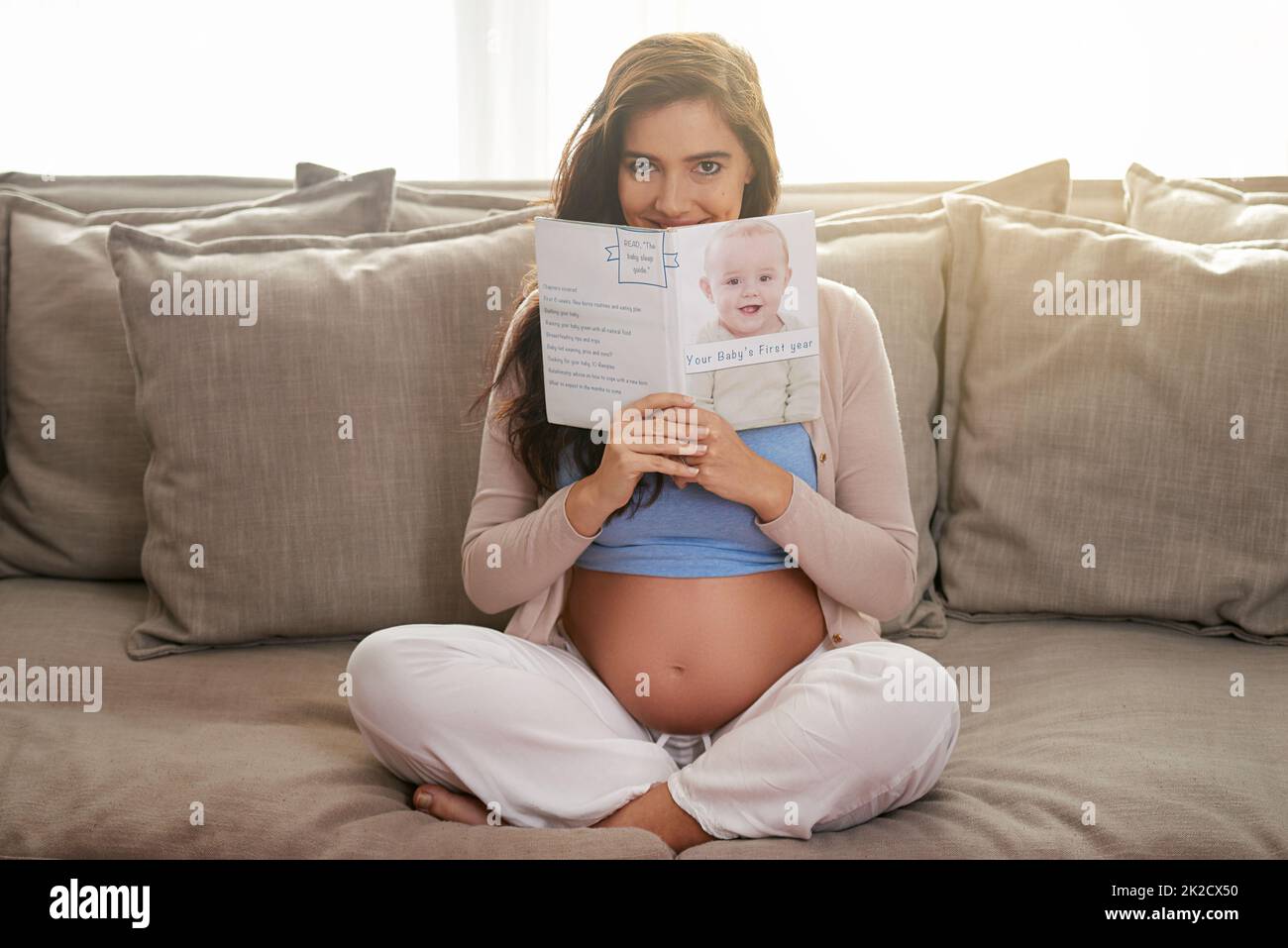 C'est un must à lire pour une mère expectative. Photo d'une jeune femme enceinte lisant un livre de bébé à la maison. Banque D'Images