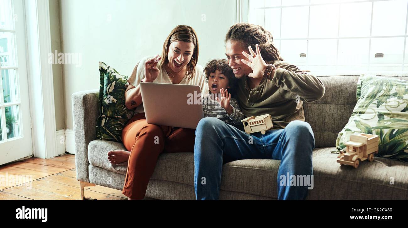 Dire bonjour au reste de la famille. Photo d'un jeune couple joyeux et de son fils ayant un appel vidéo à des parents sur un ordinateur portable tout en étant assis sur un canapé à la maison. Banque D'Images