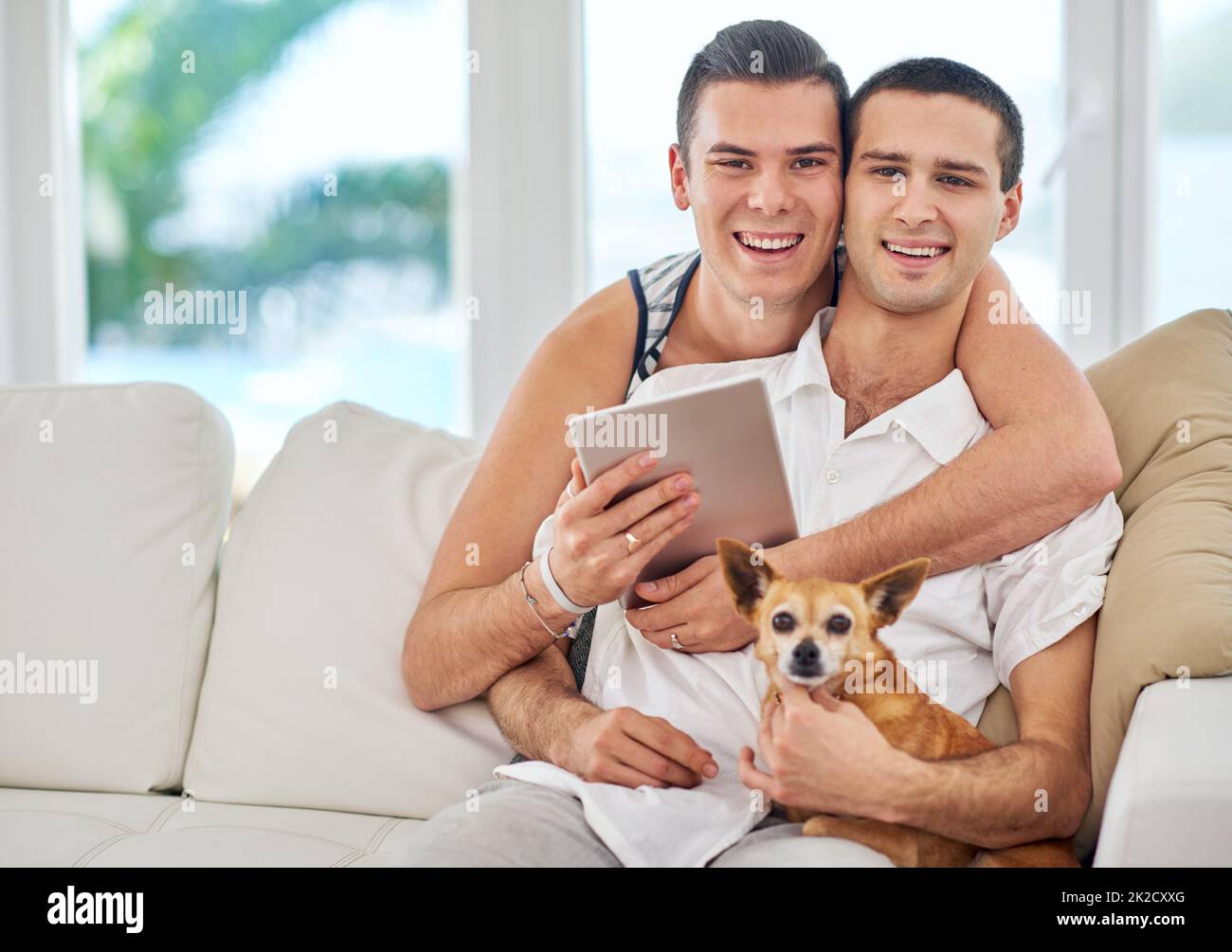 Nous étions une famille heureuse. Portrait d'un couple gay affectueux se relaxant sur le canapé avec son chien. Banque D'Images