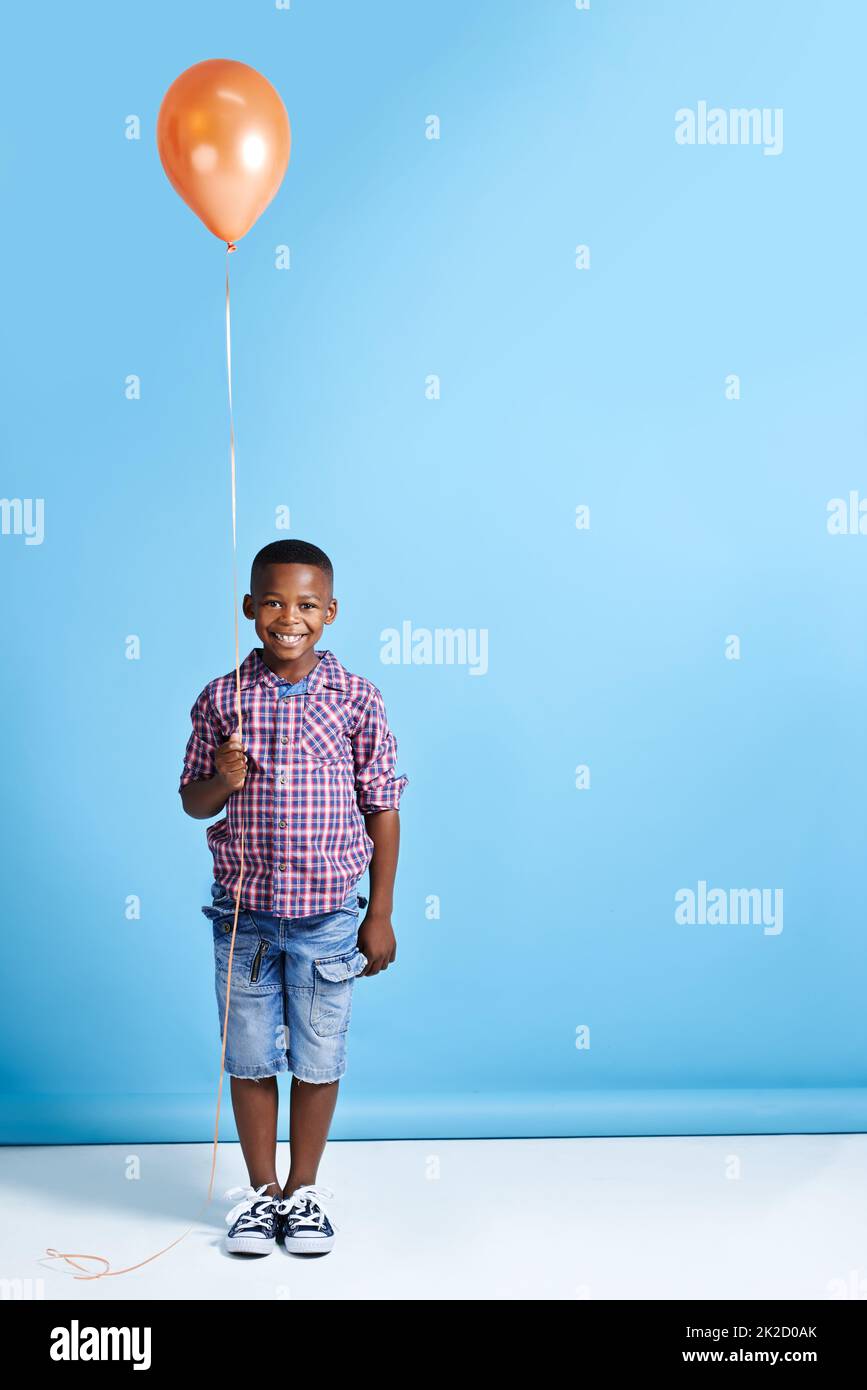 Regardez ce que j'ai obtenu. Photo d'un jeune garçon tenant un ballon sur un fond bleu. Banque D'Images