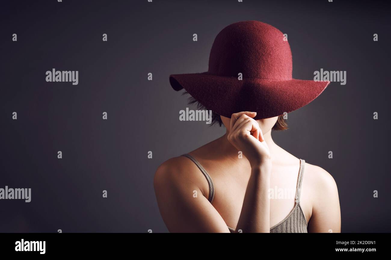 Voulez que je révèle le mystère. Photo studio d'une jeune femme méconnue couvrant son visage avec un chapeau sur fond gris. Banque D'Images