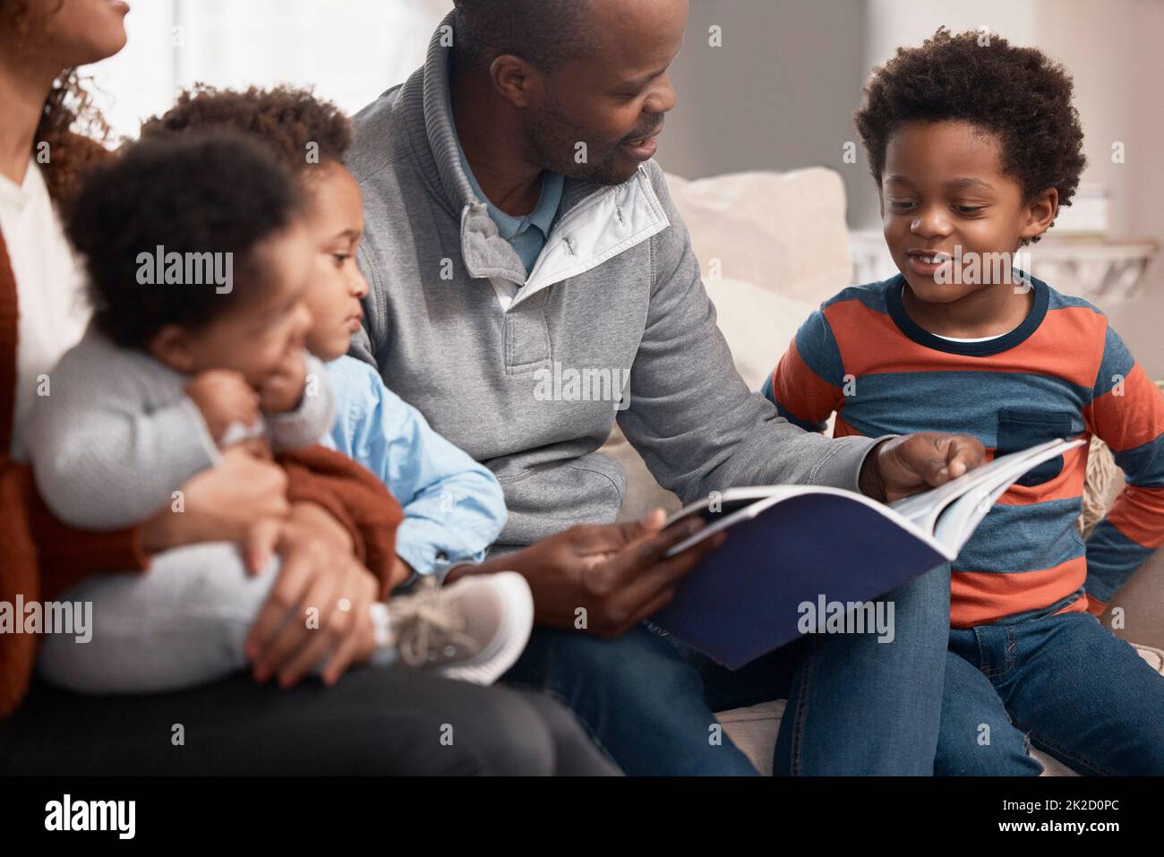 Il devient une tradition dans leur famille de lire ensemble. Photo d'un père lisant un livre à sa famille à la maison. Banque D'Images