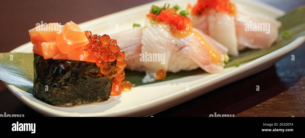 Saumon Ikura Sushi servi sur une assiette blanche décorée de feuilles de bambou vertes. Banque D'Images