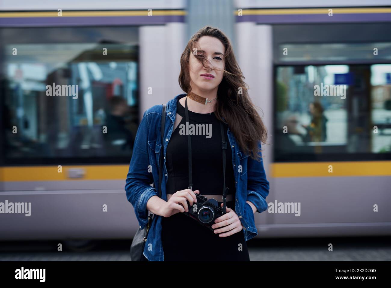 Je suis toujours à l'affût d'une occasion de prendre des photos. Portrait d'une jeune photographe féminine attirante debout dans le métro avec un train traversant en arrière-plan. Banque D'Images