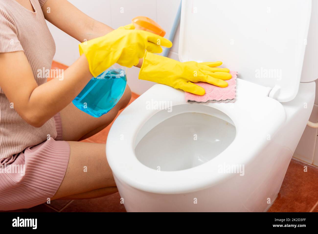 Main de femme asiatique nettoyant le siège de toilettes à l'aide d'un pulvérisateur de liquide et d'un chiffon rose essuyer les toilettes à la maison Banque D'Images