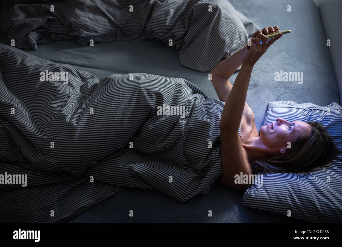Femme d'âge moyen utilisant sa tablette avant de dormir dans le lit le soir - exposition à la lumière bleue juste avant le sommeil Banque D'Images