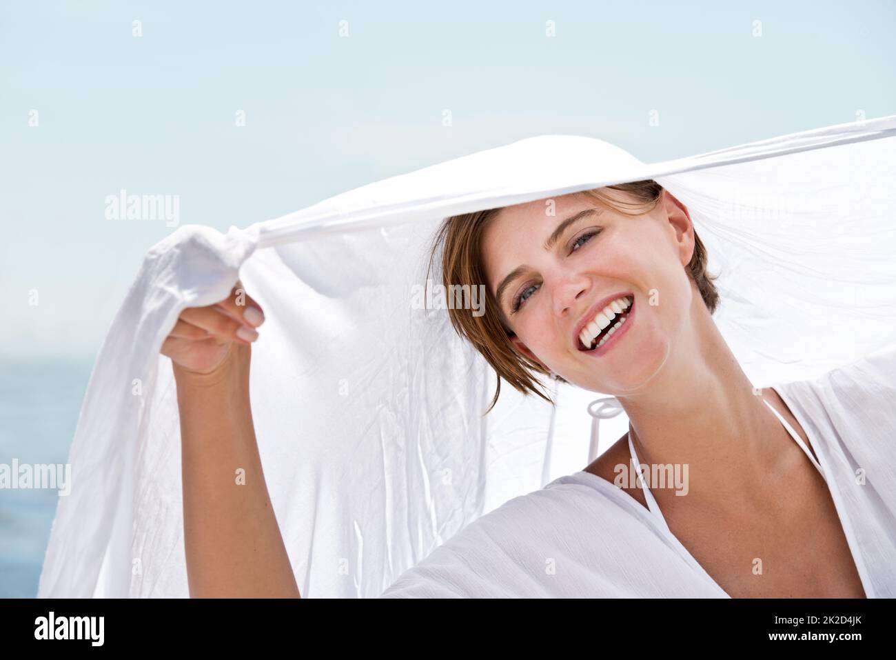 Sans soins dans le monde Une belle jeune femme tenant un sarong blanc thats soufflant dans le vent. Banque D'Images