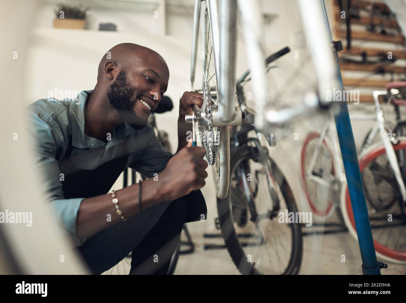 Im a presque fini de corriger cela. Photo d'un beau jeune homme qui s'est accroupi seul dans son atelier et a réparé une roue de vélo. Banque D'Images