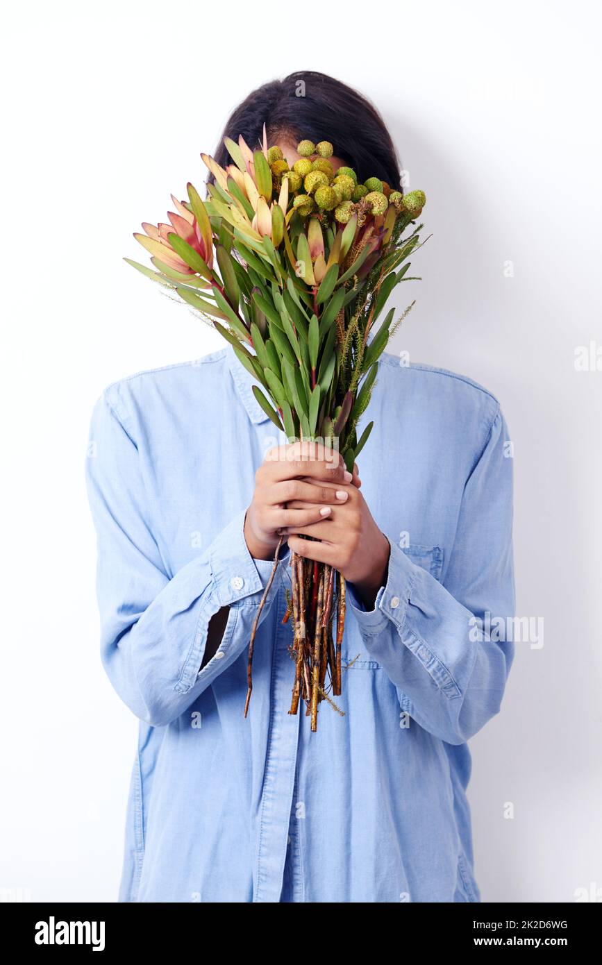 Floral et délicat. Studio photo d'une jeune femme ethnique attrayante tenant un bouquet de fleurs devant son visage. Banque D'Images