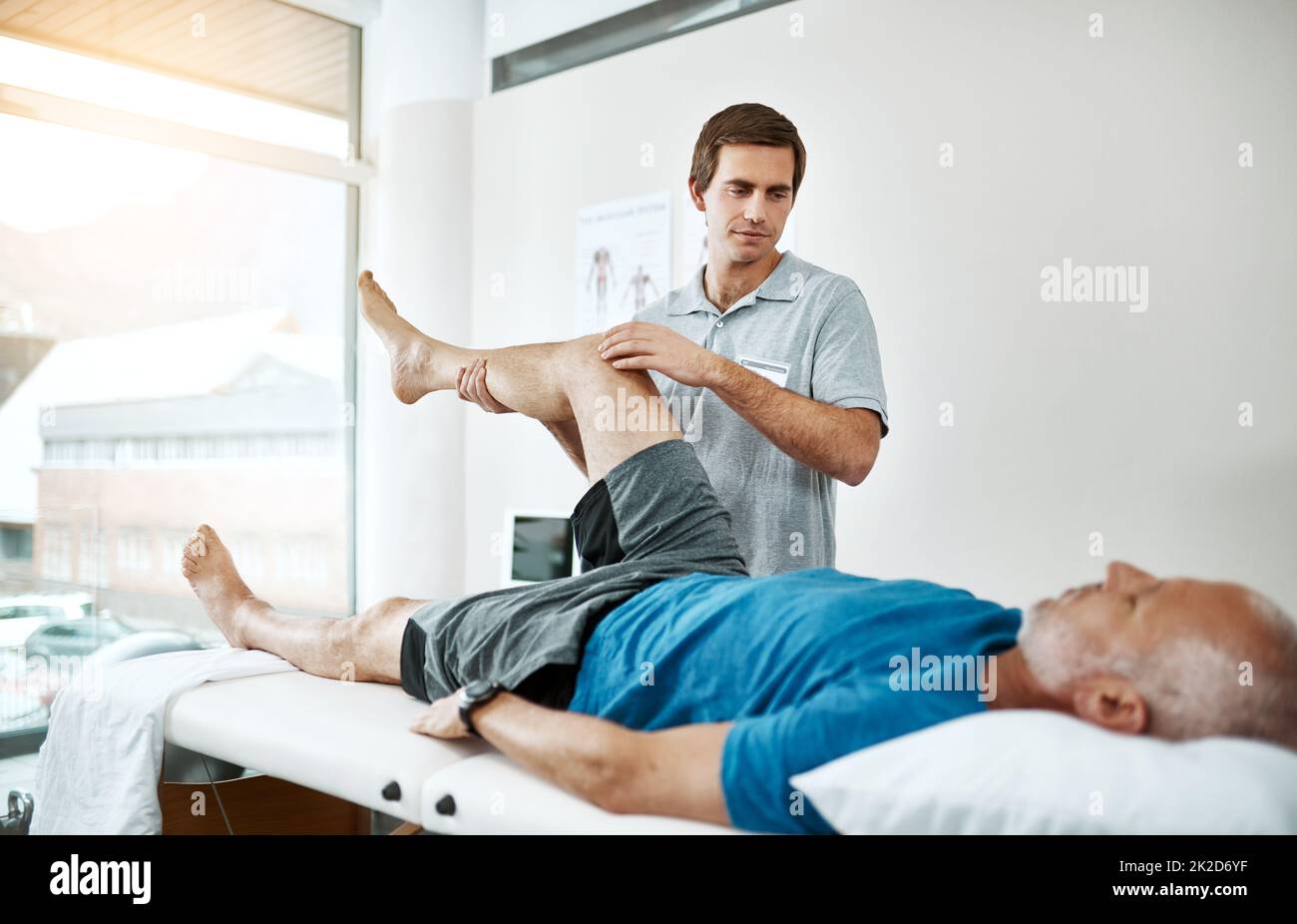La santé des clients est sa seule préoccupation. Photo d'un jeune kinésithérapeute masculin aidant un client avec des exercices de jambe qui se trouvent sur un lit. Banque D'Images