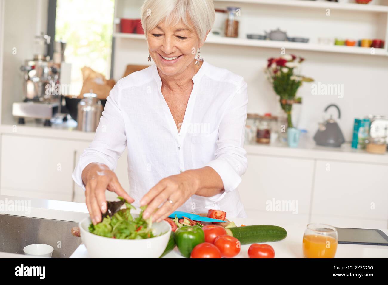 Le secret de la vitalité est une alimentation saine. Prise de vue d'une femme âgée qui fait une salade dans sa cuisine. Banque D'Images