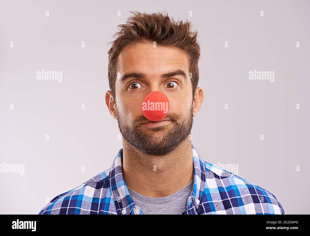Rudolph n'est pas disponible, alors il ne vous reste pas à guider votre traîneau. Photo studio d'un beau homme portant un nez rouge sur fond gris. Banque D'Images