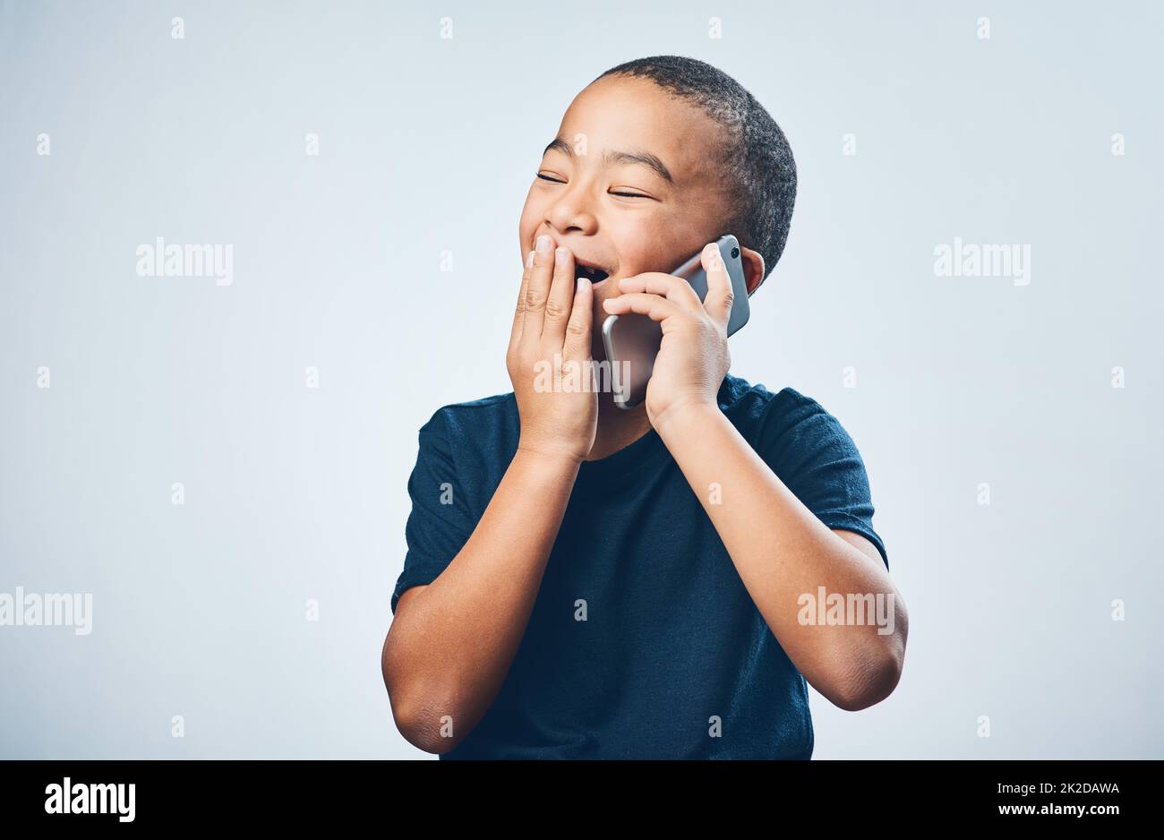 Un appel de grand-mère lui donne toujours les rigoles. Photo en studio d'un petit garçon à l'apparence stupéfaite en utilisant un smartphone sur fond gris. Banque D'Images