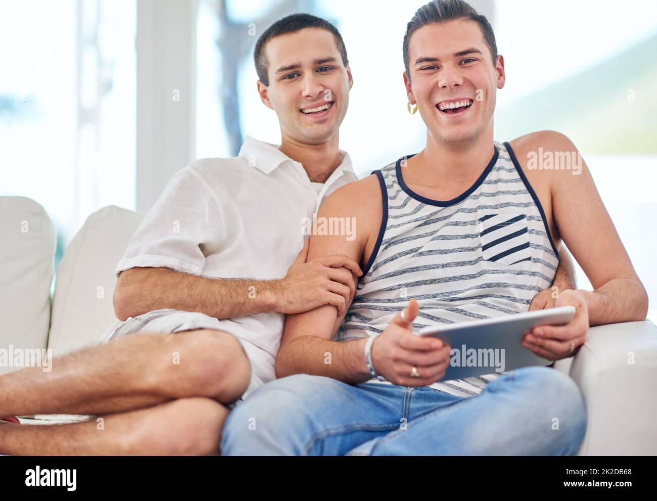 Chaque jour est spécial. Portrait d'un couple gay utilisant une tablette numérique tout en se relaxant sur le canapé à la maison. Banque D'Images