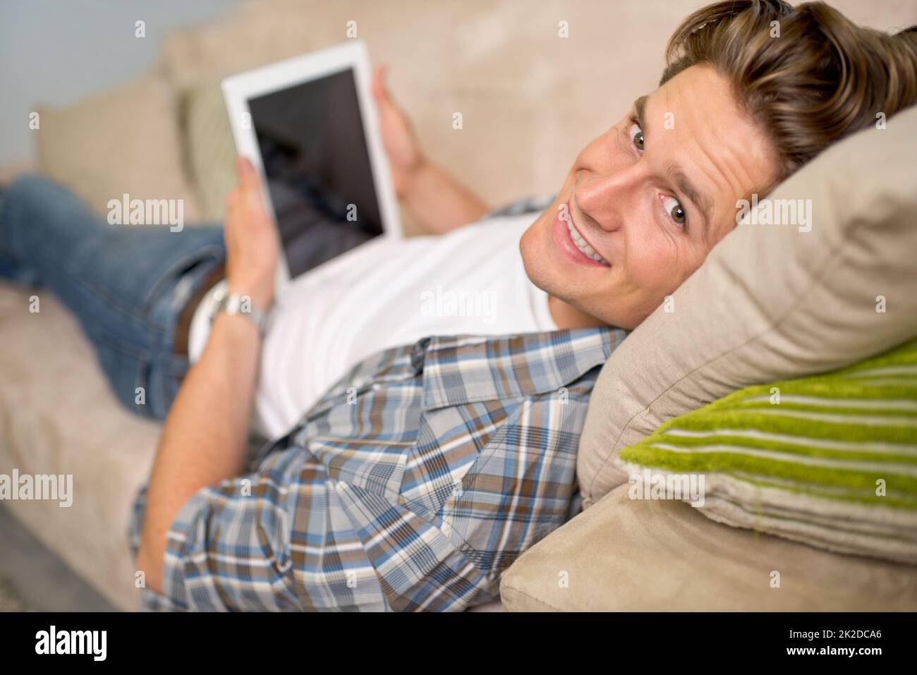 Confort de créature Prise de vue d'un beau jeune homme à l'aide de sa tablette numérique tout en se relaxant sur le canapé. Banque D'Images