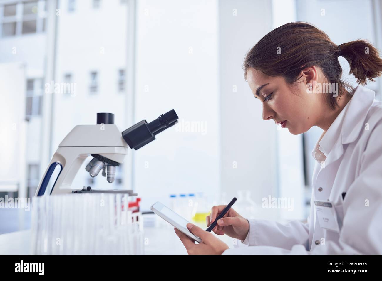 La recherche n'est qu'une partie du travail. Photo d'une jeune scientifique travaillant sur une tablette numérique tout en étant assise dans un laboratoire. Banque D'Images