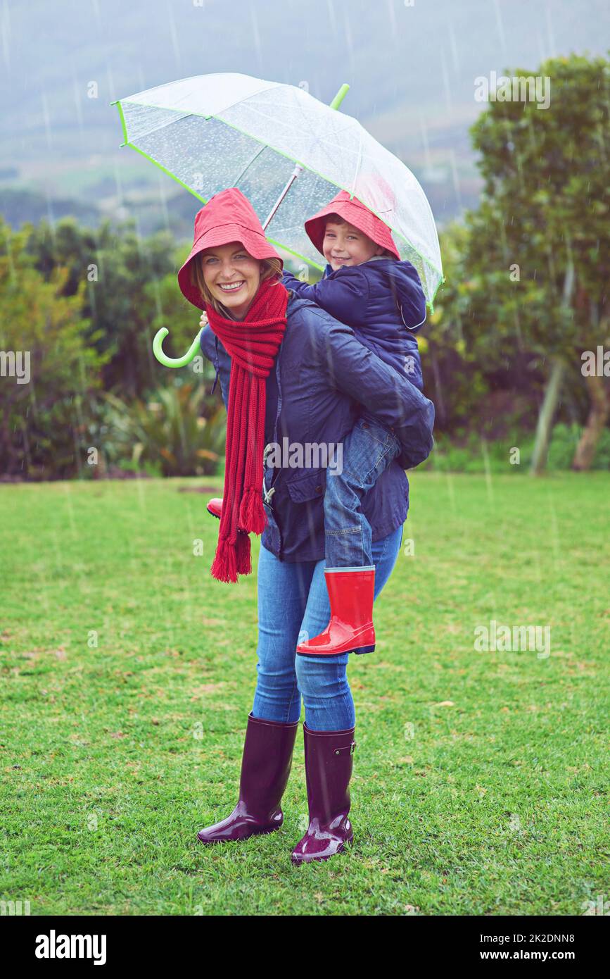 Ludique sous la pluie. Portrait court d'une mère portant son fils sur le dos à l'extérieur sous la pluie. Banque D'Images