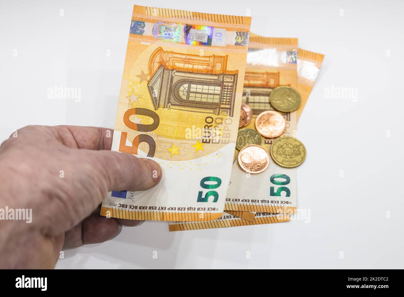 Main d'homme tenant une note de 50 euros et des pièces de monnaie en arrière-plan Banque D'Images
