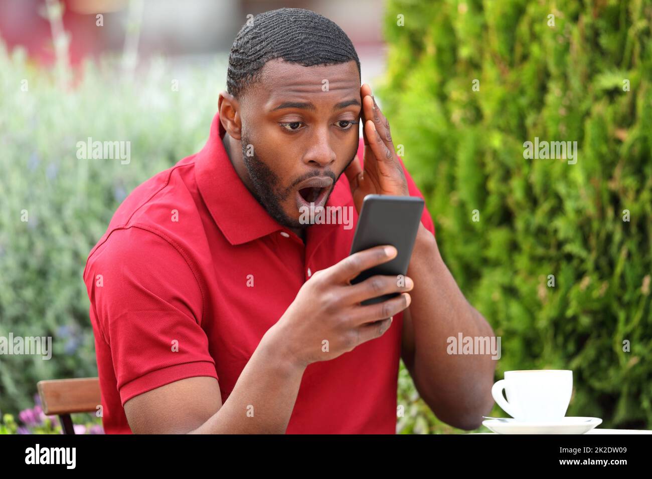 Un homme émerveillé avec une peau noire vérifiant le téléphone dans un bar Banque D'Images