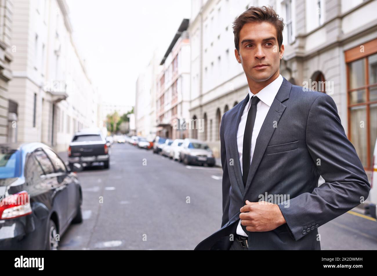 La vie et le style dans la ville. Un beau homme d'affaires en costume qui traverse une rue de la ville. Banque D'Images