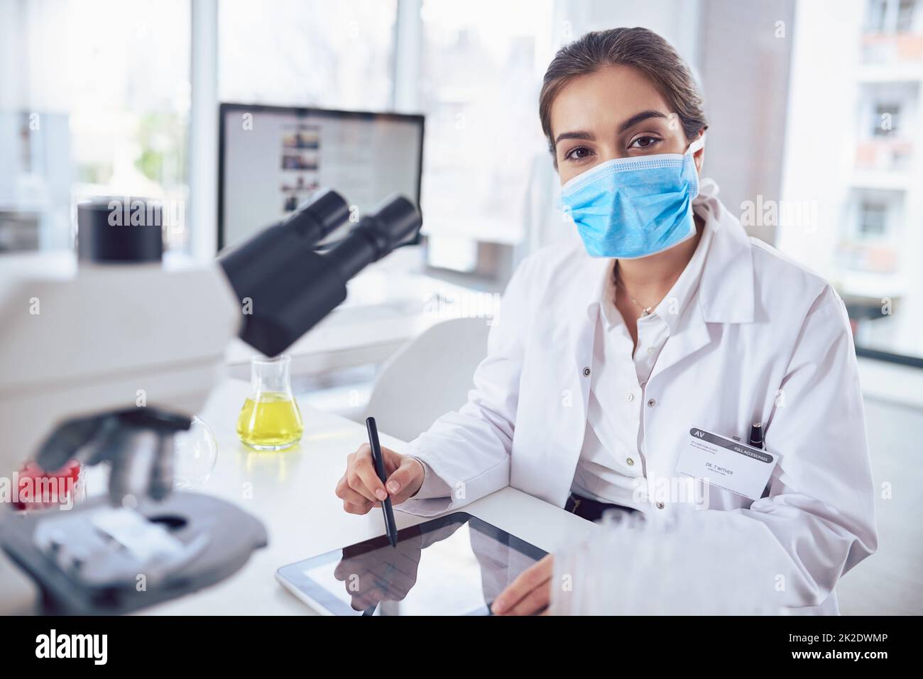 Juste un autre jour dans le laboratoire. Portrait d'une jeune scientifique confiante portant un masque chirurgical et travaillant sur une tablette numérique tout en regardant la caméra dans un laboratoire. Banque D'Images