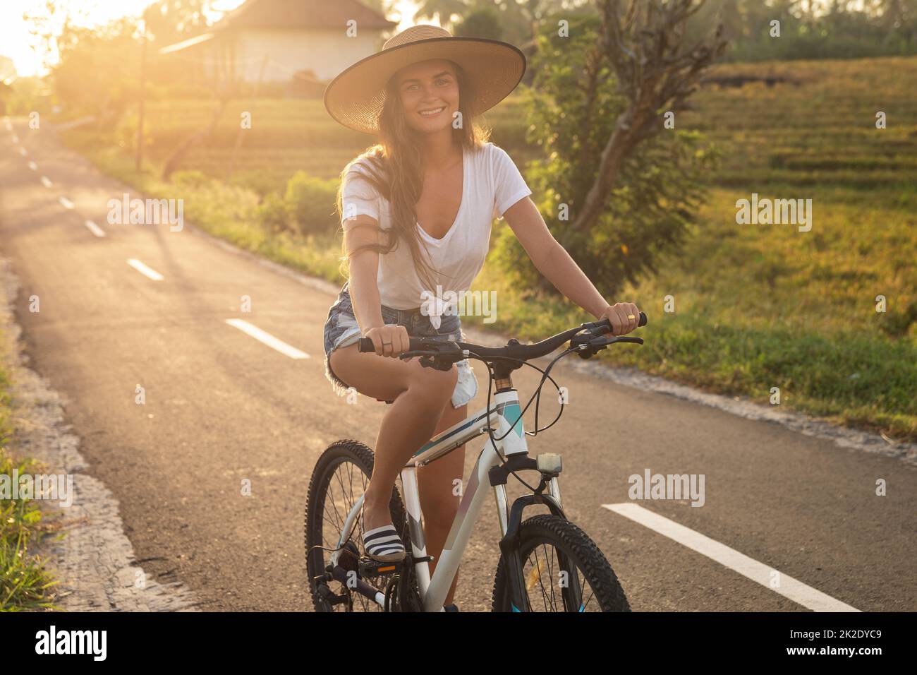 La femme est à vélo par la route de campagne étroite Banque D'Images