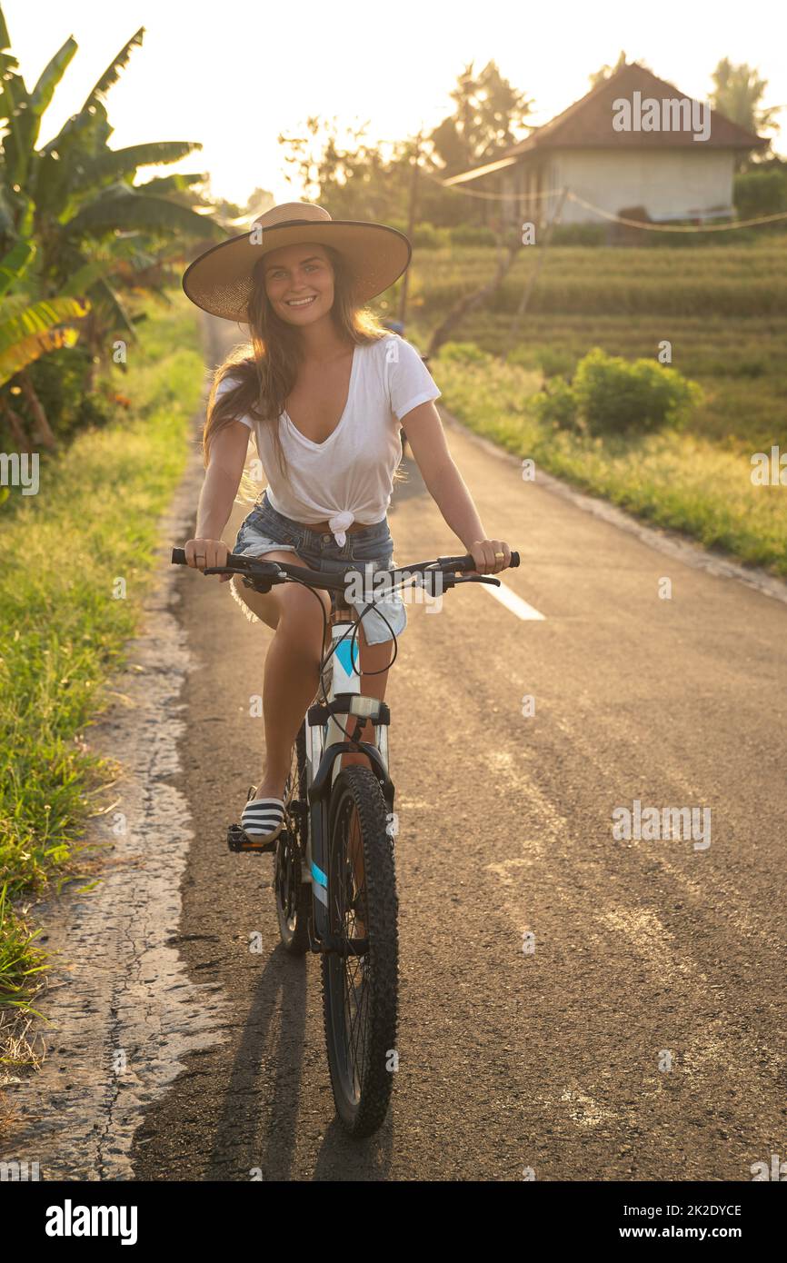 La femme est à vélo par la route de campagne étroite Banque D'Images