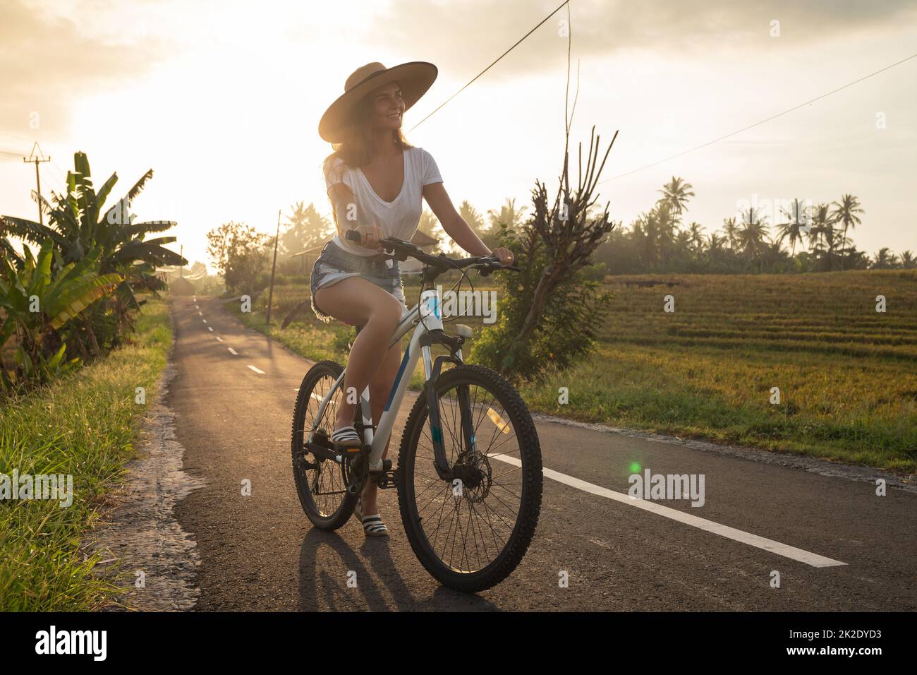 La femme est à vélo par la route de campagne étroite Banque D'Images