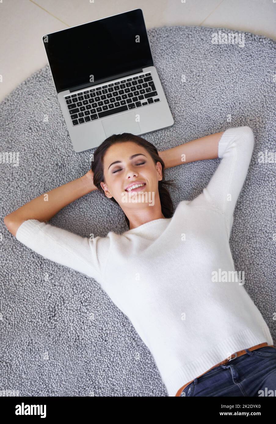 Laisser mon travail s'inquiéter de lui-même pour un changement. Photo d'une jeune femme allongé sur un tapis à côté d'un ordinateur portable. Banque D'Images