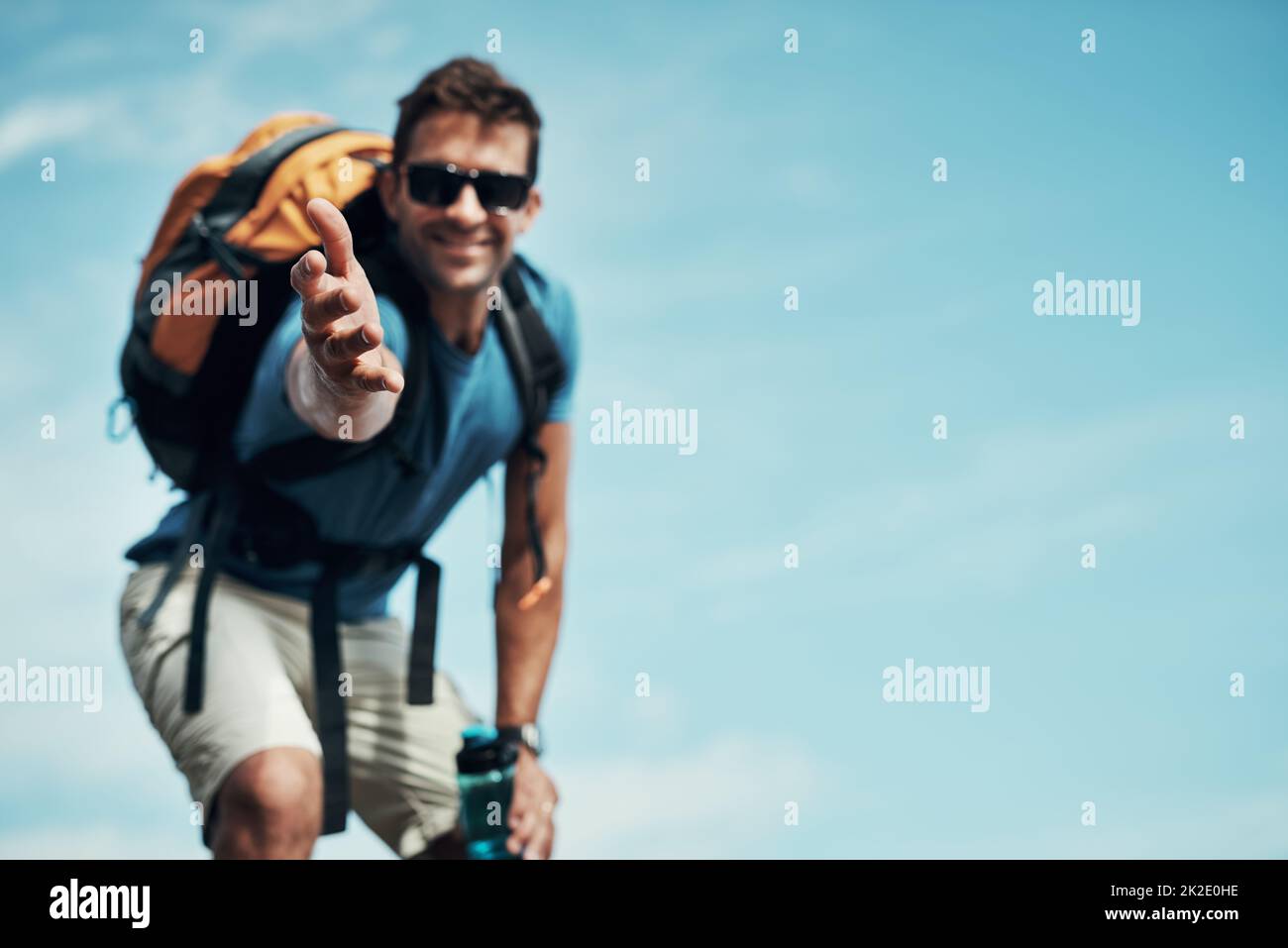 Venez avec moi. Portrait d'un jeune homme joyeux qui s'étire la main pour aider à faire une randonnée en montagne. Banque D'Images