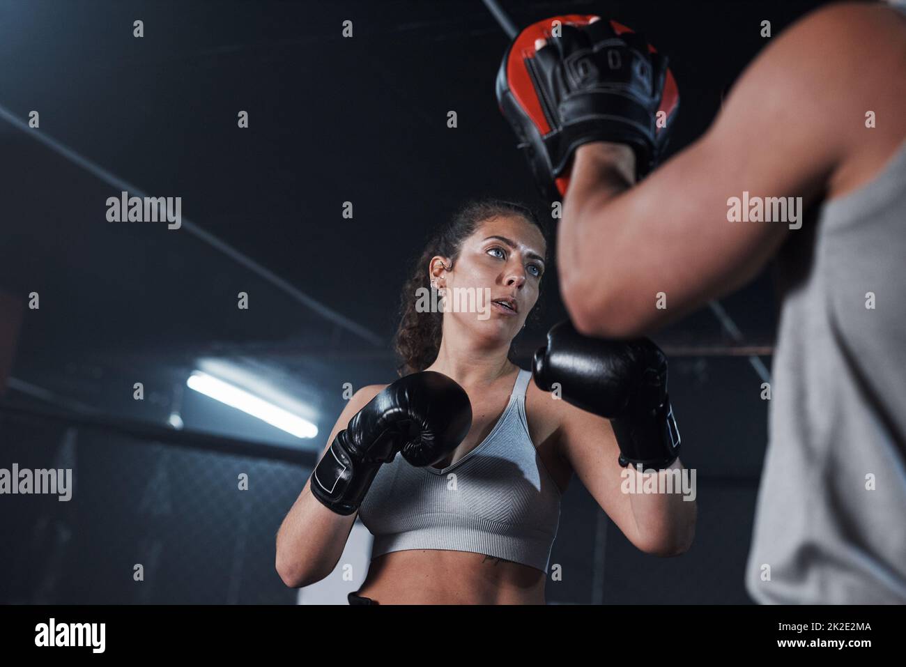 Libérez votre bête intérieure. Photo d'une jeune femme pratiquant avec son entraîneur dans un gymnase de boxe. Banque D'Images